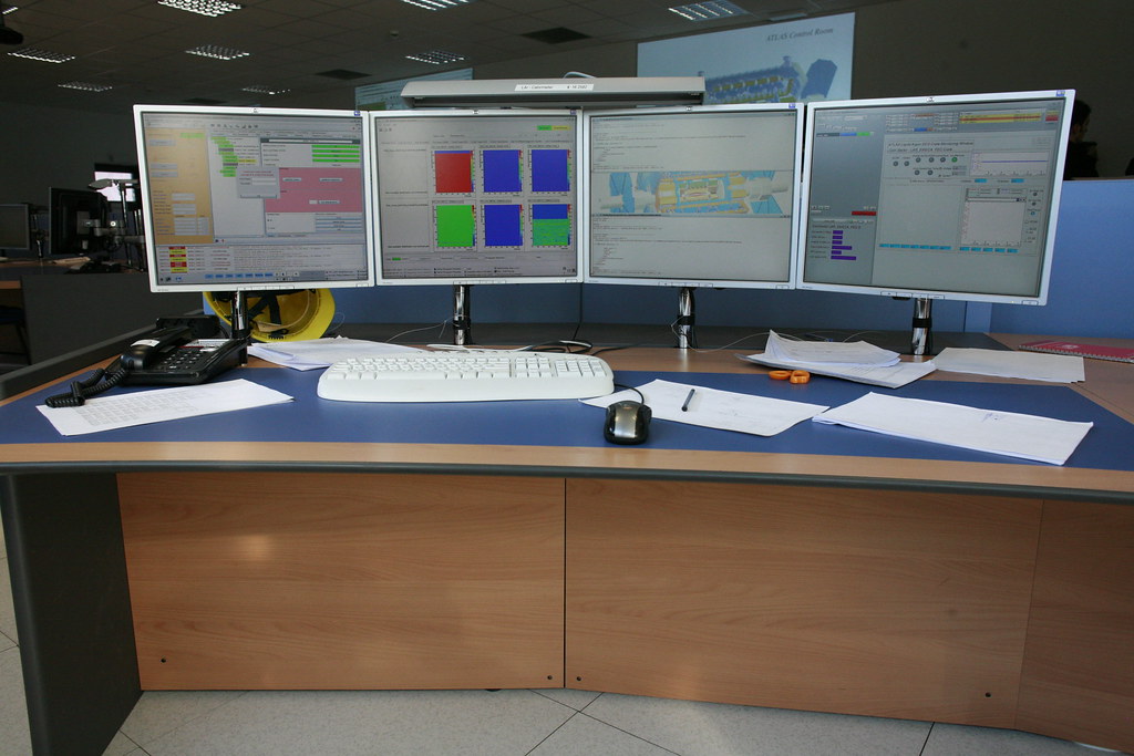 Multi-screen operations room with desks and monitoring displays.